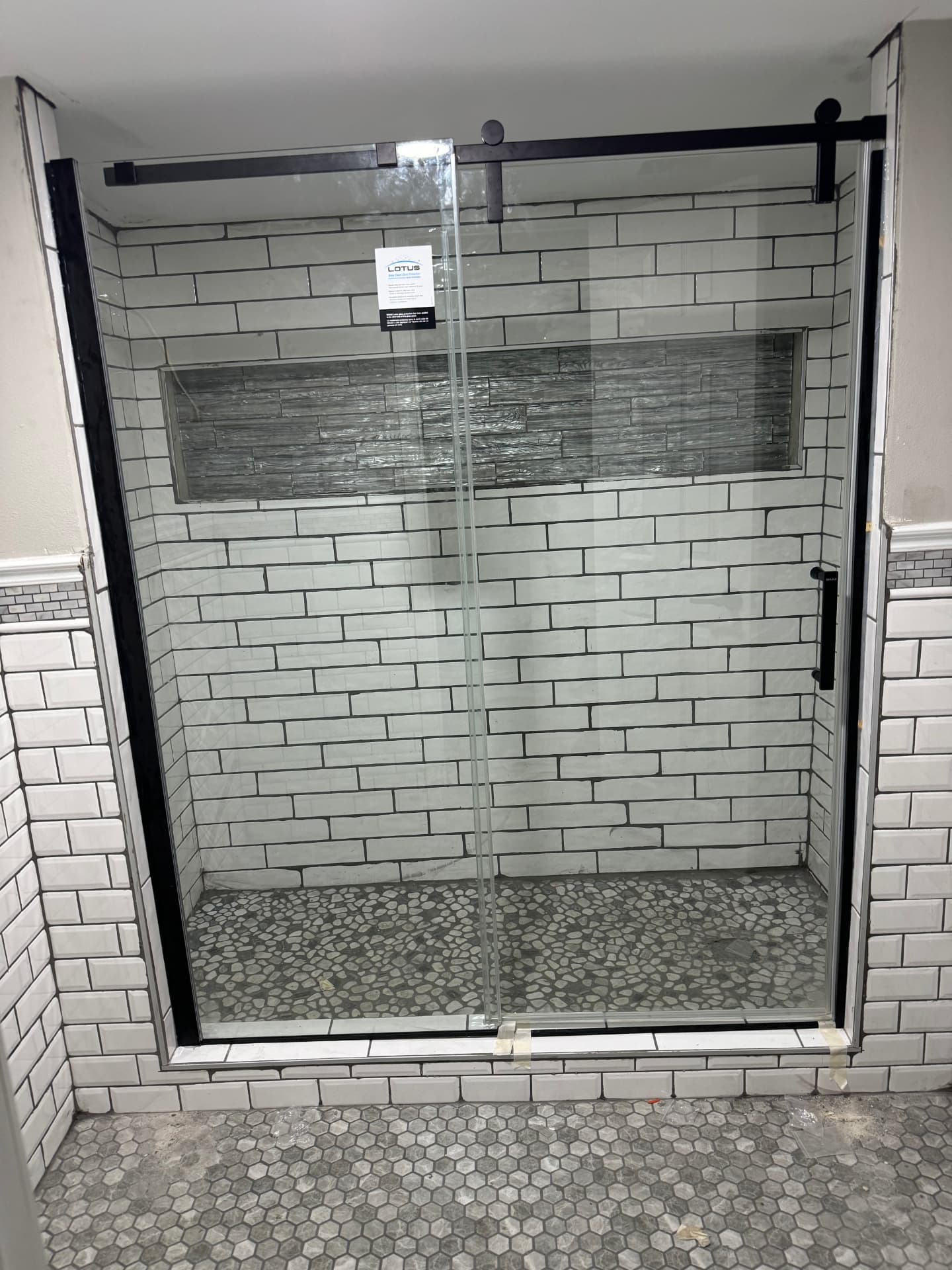 Remodeled tiled shower with glass sliding doors and black hardware